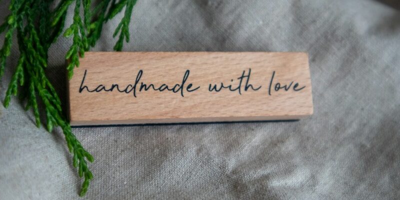 Wooden sign reading "handmade with love", framed by a cedar bough.